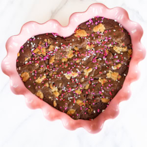 Heart-shaped brookie with pink and white sprinkles in a pink scalloped dish on a marble surface.