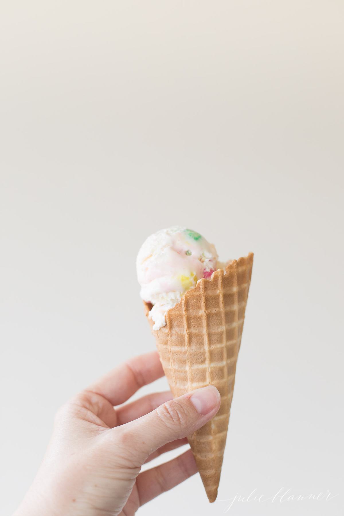 A hand holding a bubble gum ice cream scoop inside a waffle cone. 