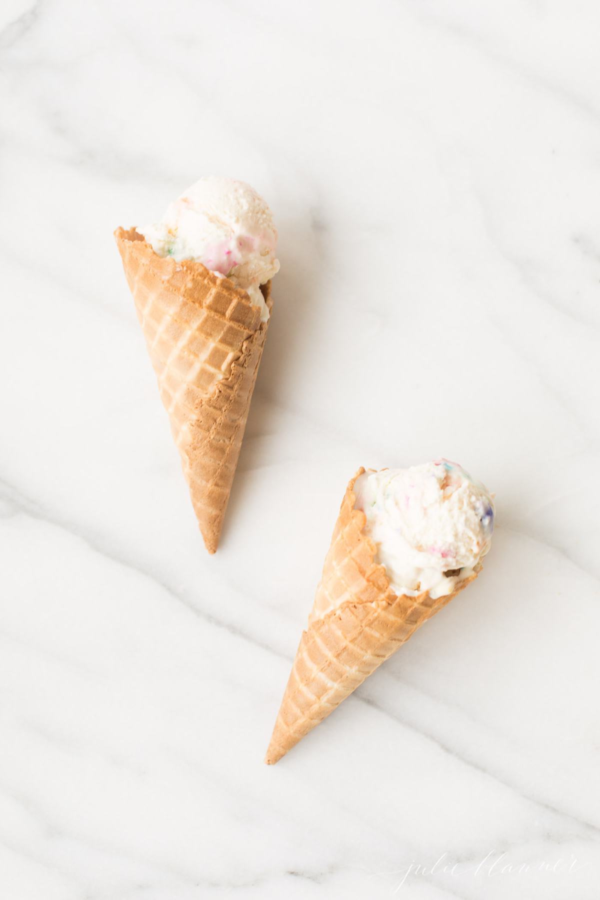 No churn bubble gum ice cream in two waffle cones on a marble countertop. 