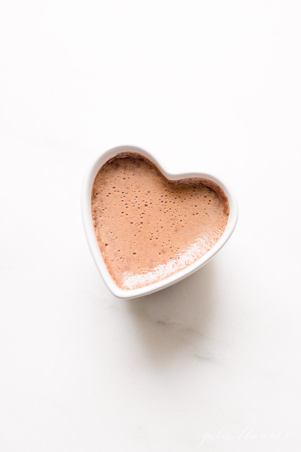 A chocolate pot de creme in a small heart shaped ceramic pot on a marble surface