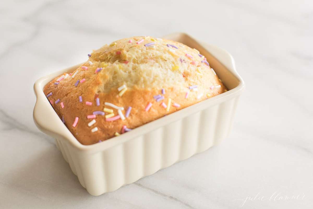 A funfetti bread recipe in a mini white loaf pan on a white marble surface.
