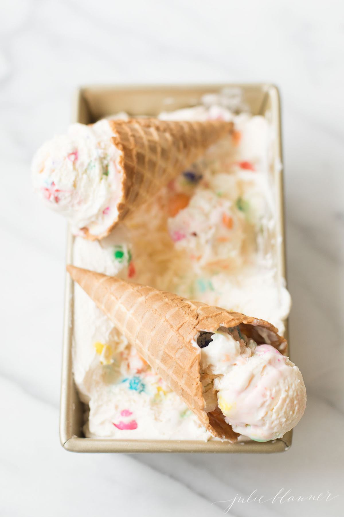 Bubble gum ice cream in a gold loaf pan on a marble countertop. 