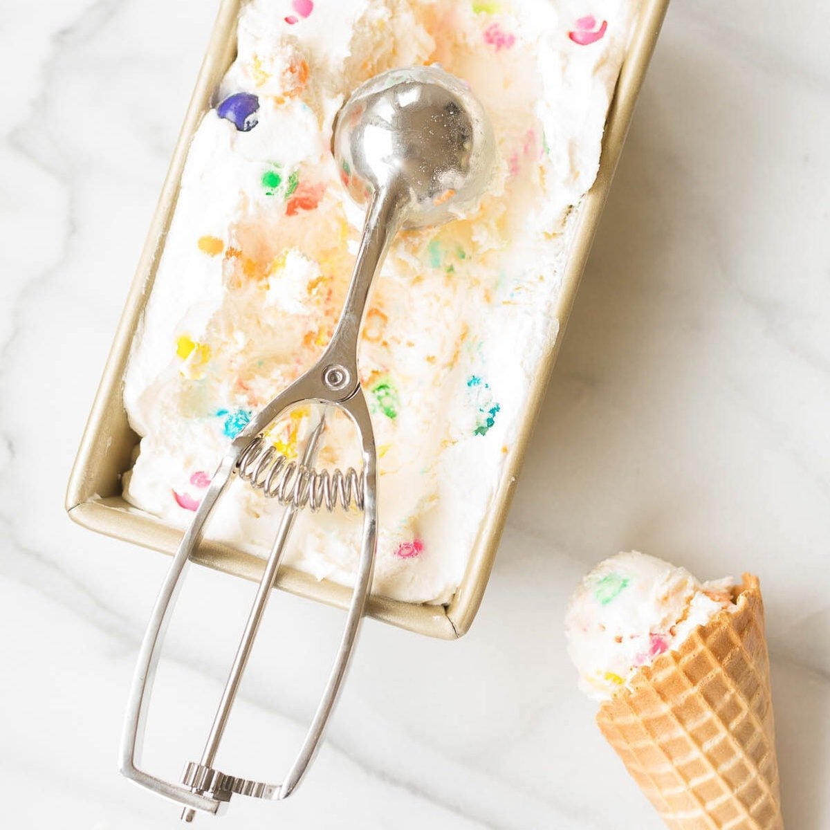 Bubble gum ice cream frozen into a gold loaf pan, with a cone to the side.