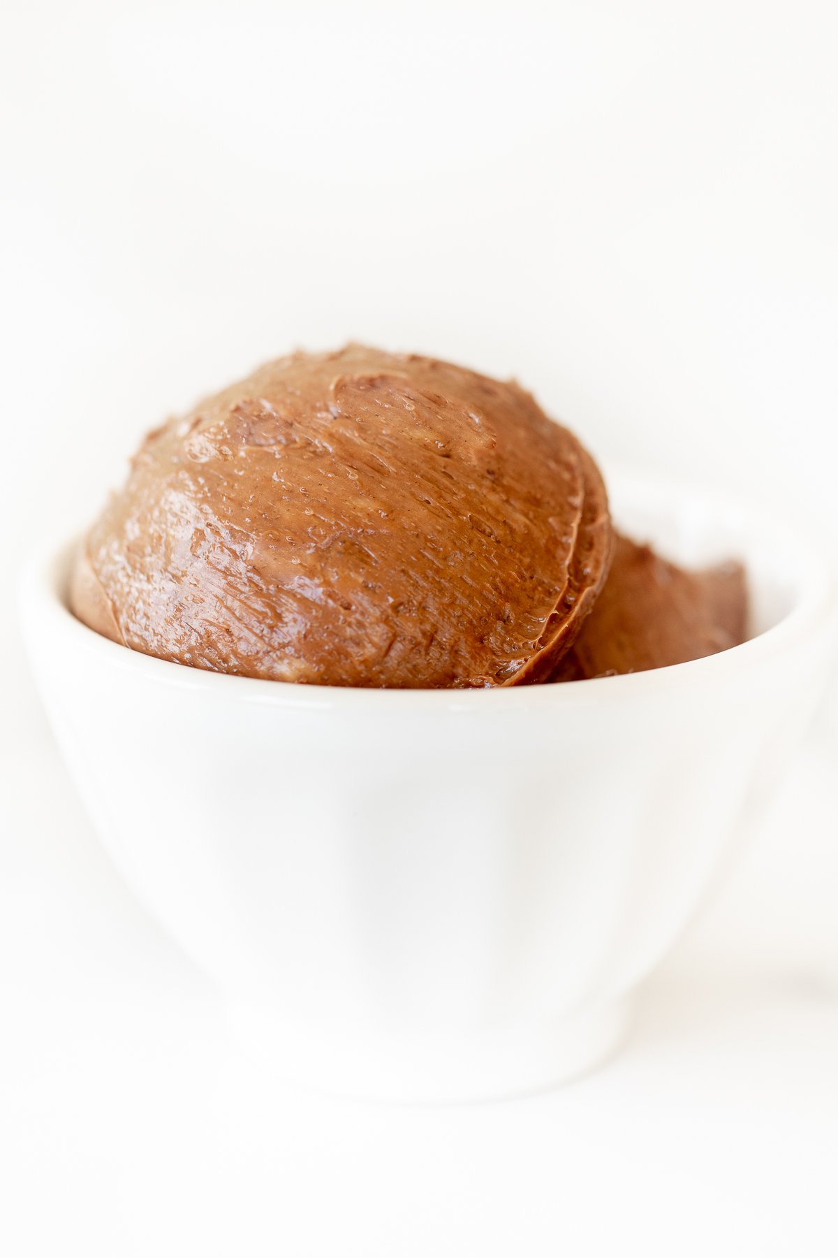 A small white bowl full of chocolate butter, on a marble surface.