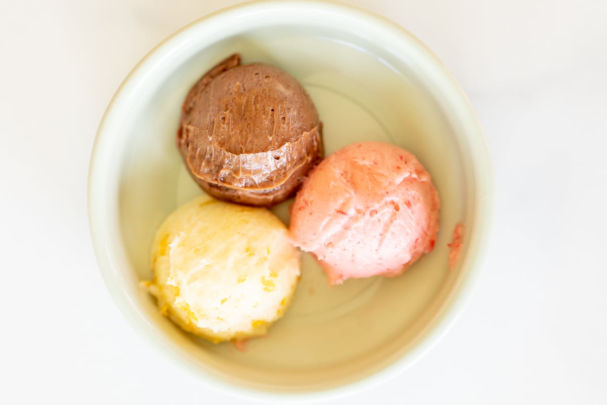 A small white bowl with a scoop of chocolate butter, strawberry butter and orange butter.