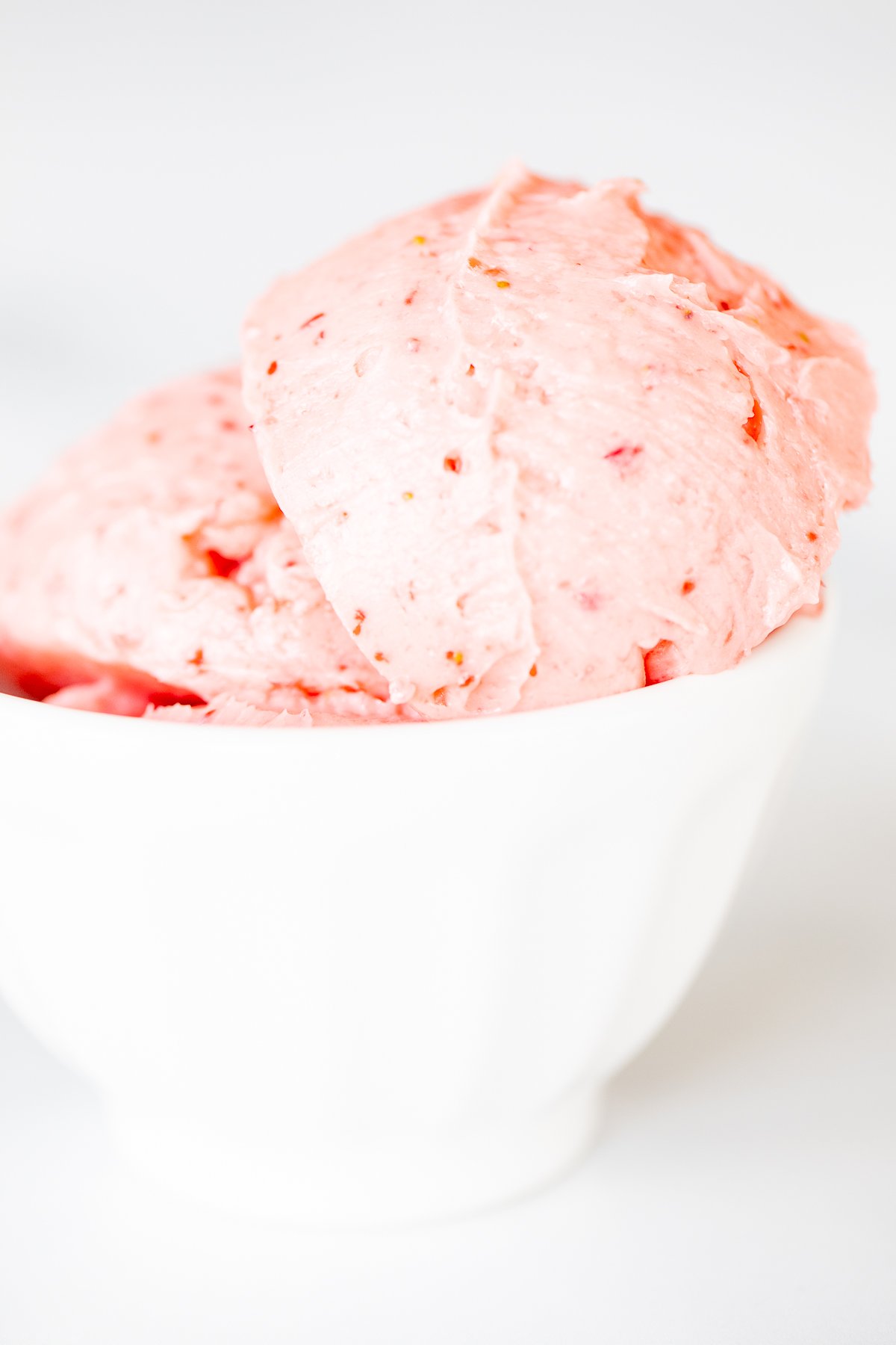 A small white bowl full of pink toned strawberry butter, on a marble surface.
