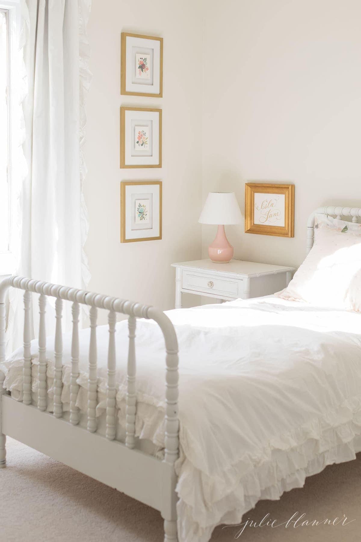 a white girl's bedroom with gold framed art work.