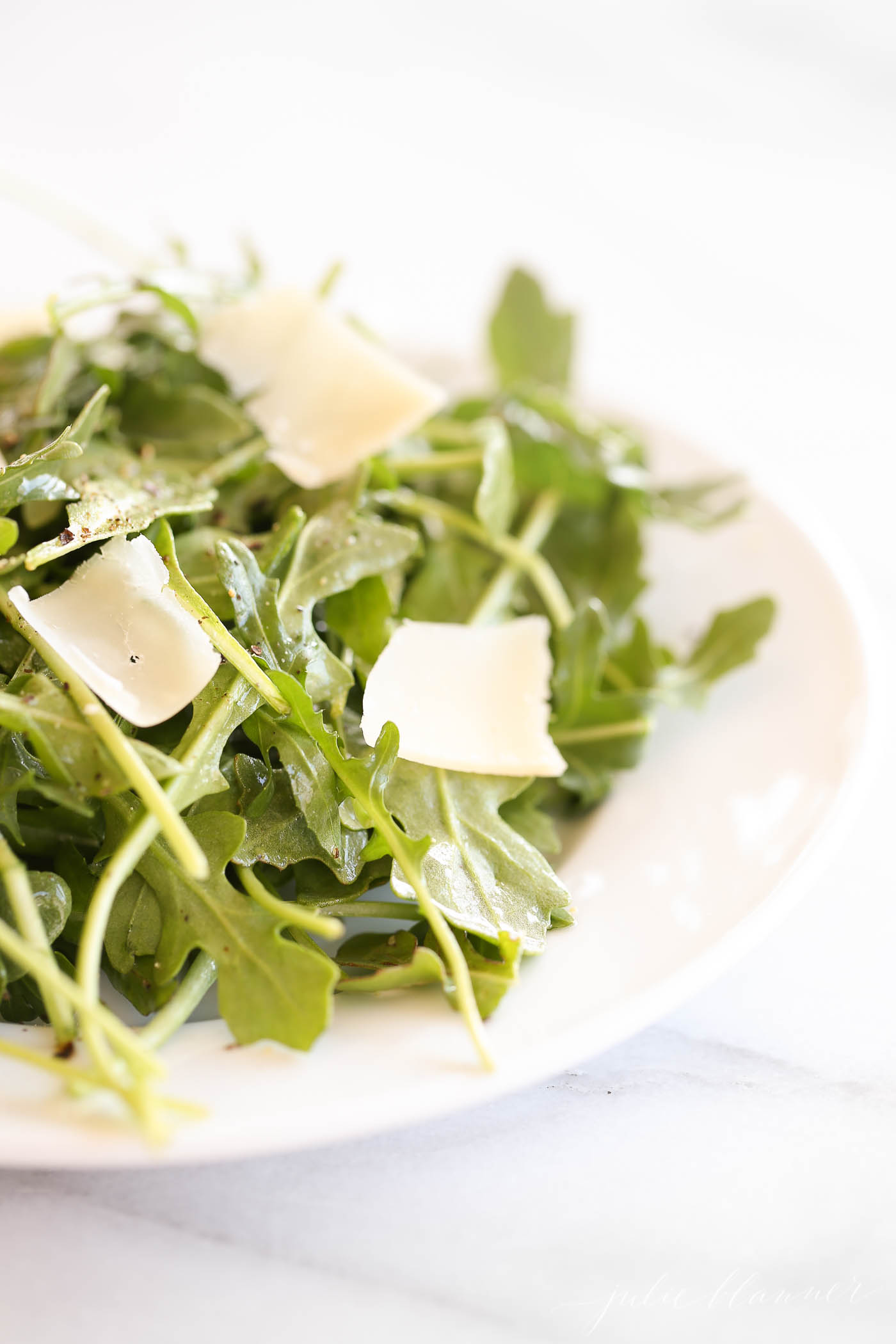 arugula salad recipe with parmesan shavings on white plate