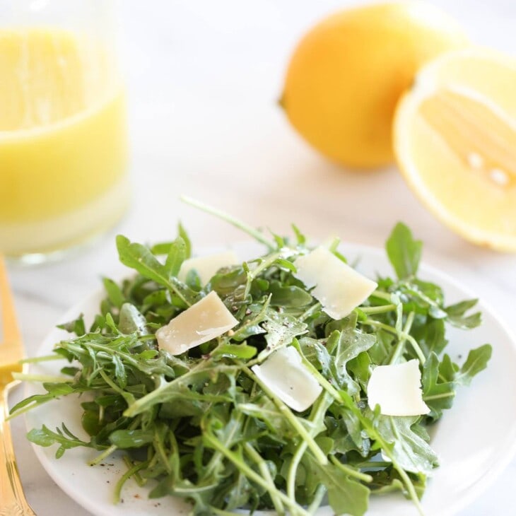 arugula salad recipe on white plate with parmesan and lemon vinaigrette