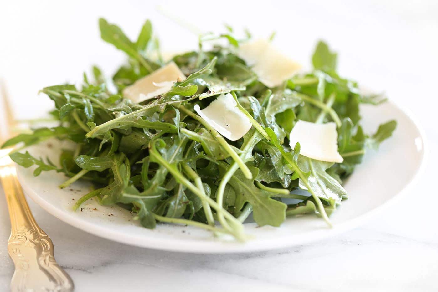 arugula salad recipe with parmesan shavings on white plate