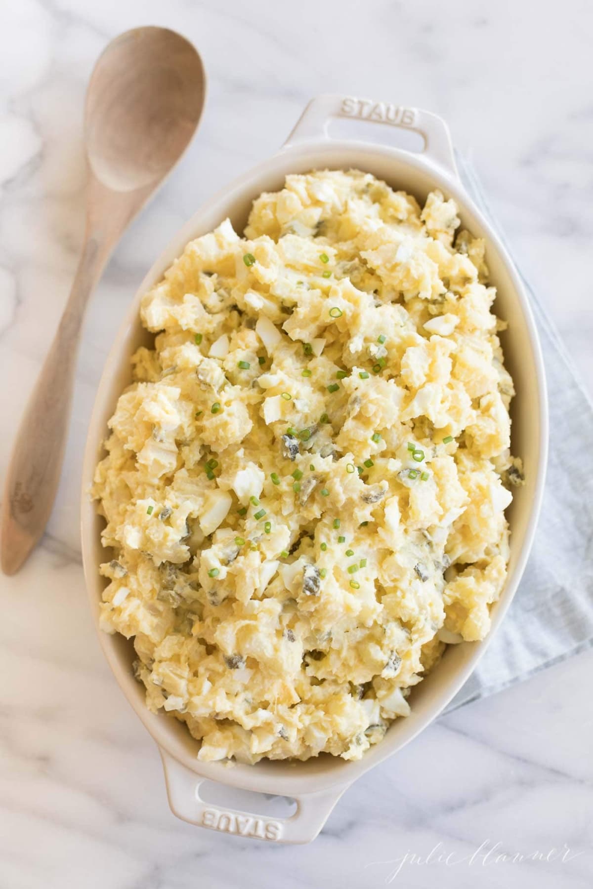 homemade potato salad with eggs in a white casserole dish with wooden spoon