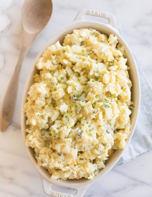 homemade potato salad with eggs in a white casserole dish with wooden spoon