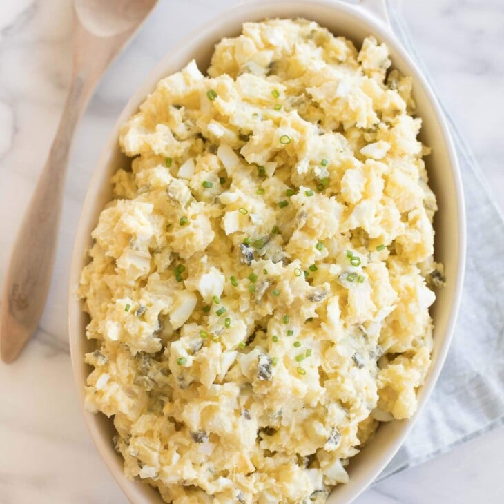 homemade potato salad with eggs in a white casserole dish with wooden spoon