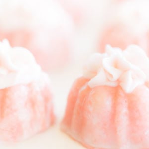 Close-up of pink champagne cupcakes with delicate white icing flowers on top, set against a soft, light background.