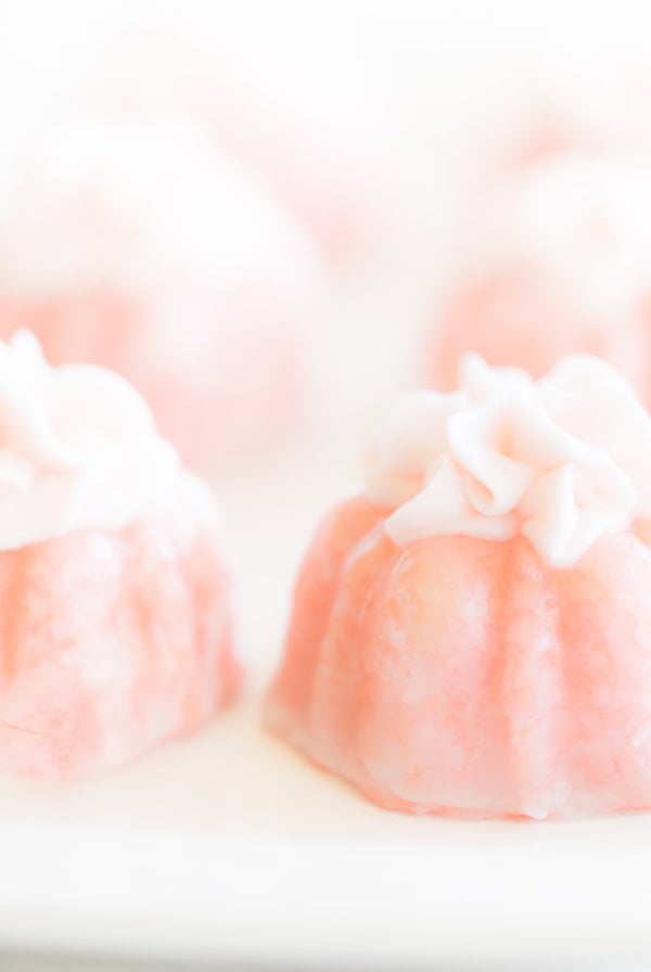 Close-up of pink champagne cupcakes with delicate white icing flowers on top, set against a soft, light background.