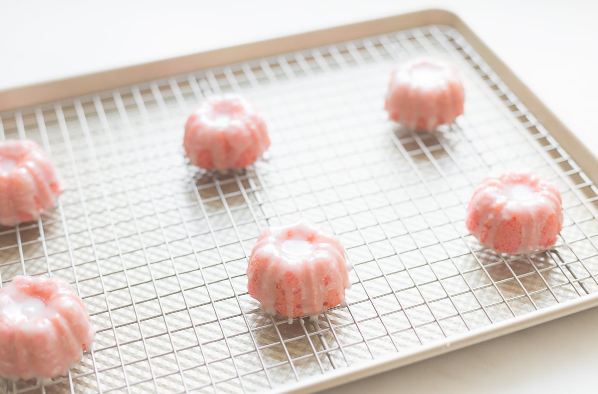 Pink champagne cupcakes on a wire baking sheet in a gold baking pan. 