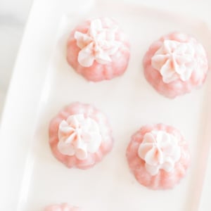 Five pink champagne cupcakes with white floral garnishes on a white rectangular plate.