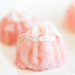 Two pink champagne cupcakes with white floral designs, presented on a light background.
