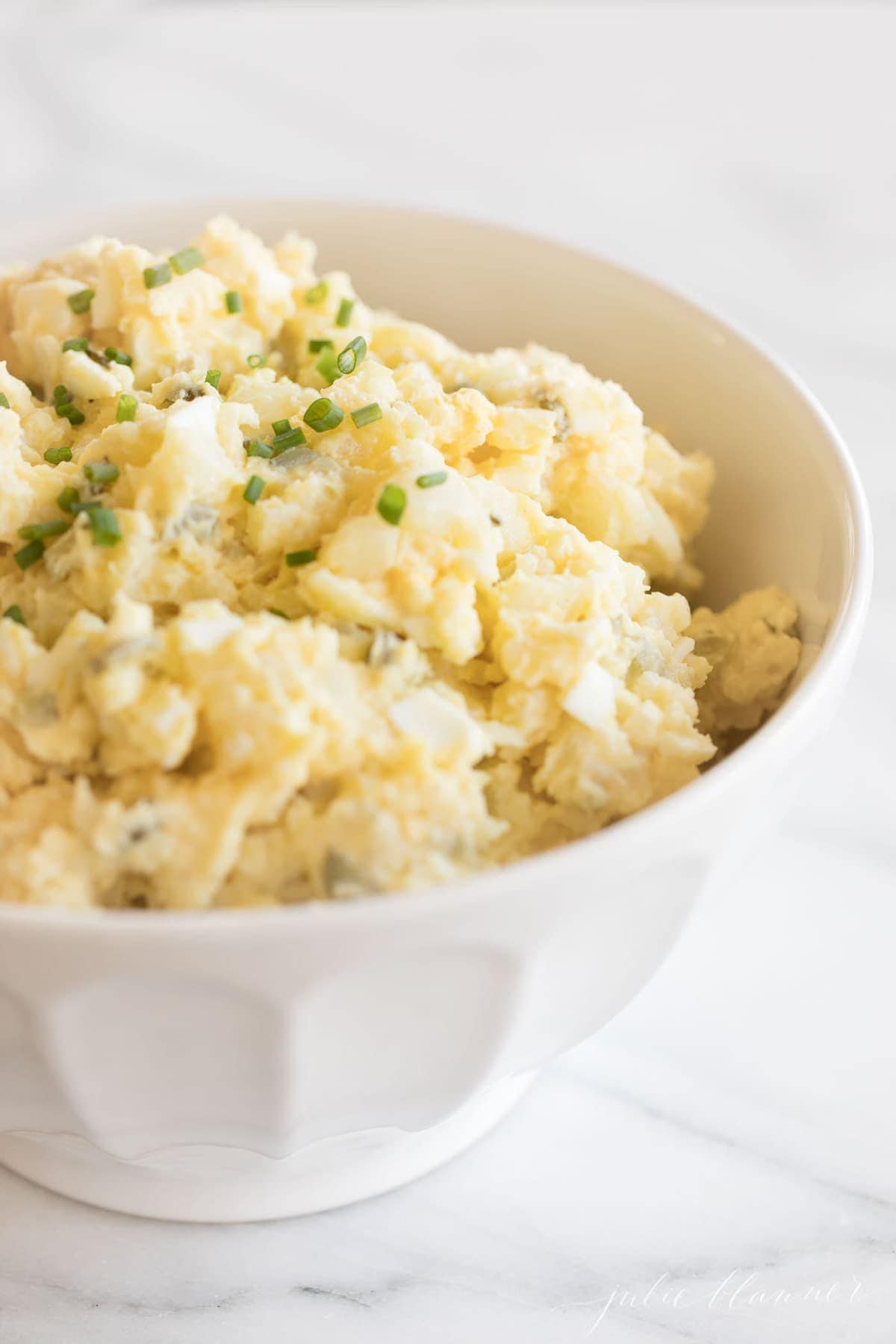 homamade potato salad with eggs in a white bowl