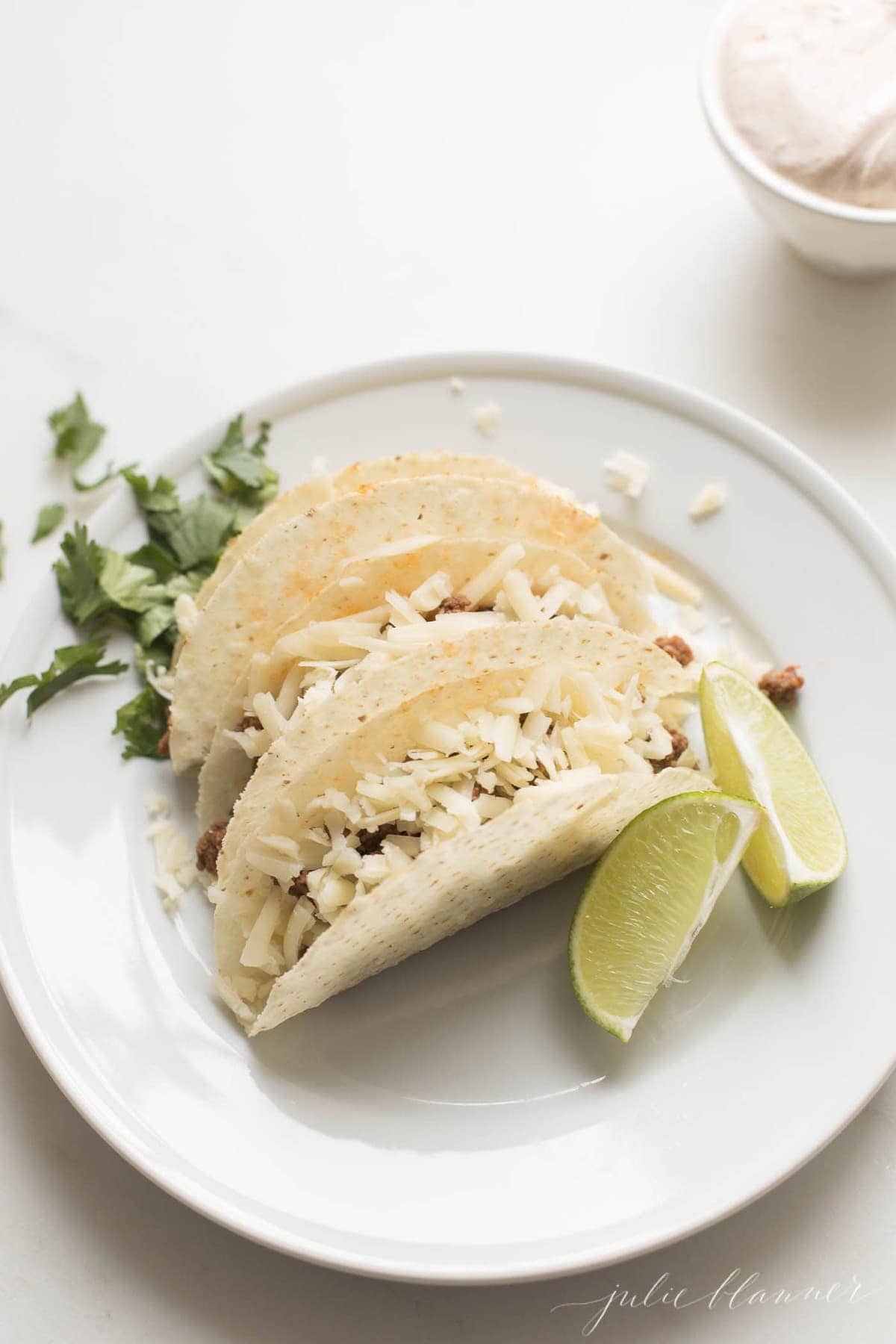 beef taco recipe on white plate with lime wedges and cilantro