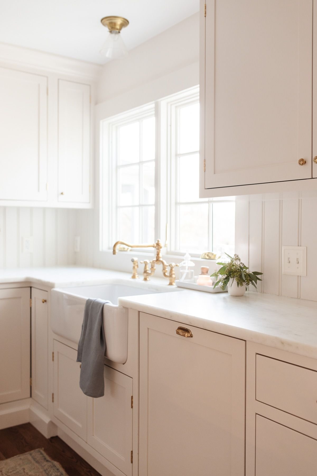 A white farm sink with a brass faucet and eucalytpus in a vase