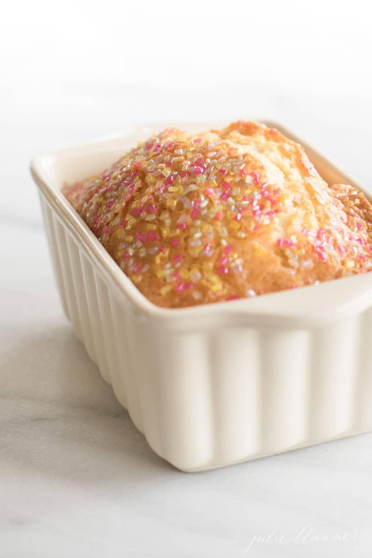 A white mini loaf pan filled with quick bread topped with sugar crystals