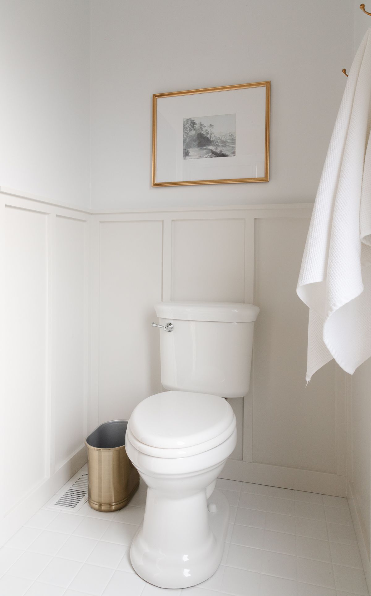 A small bathroom with white tile floors and gray board and batten on the walls