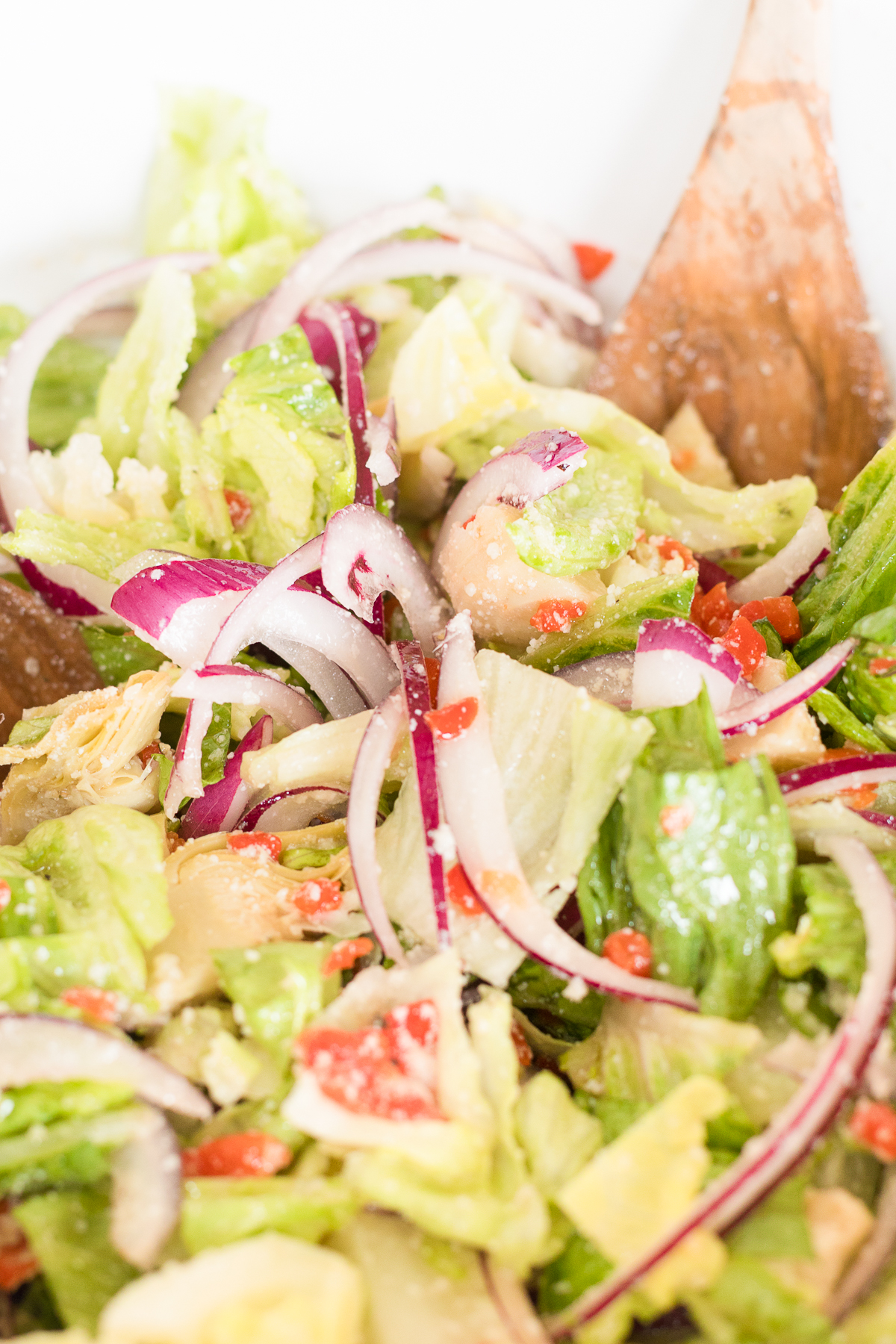 A fresh Italian salad mixed with lettuce, red onions, and tomatoes, partially tossed with wooden utensils.