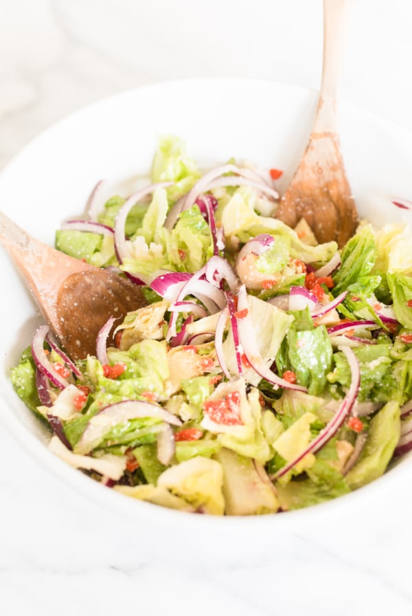 Fresh Italian vegetable salad with sliced red onions and wooden serving utensils, topped with Italian salad dressing.