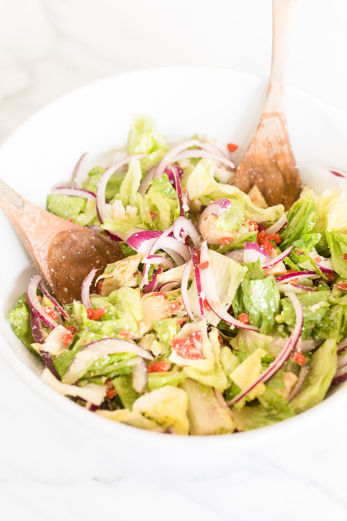 Fresh Italian vegetable salad with sliced red onions and wooden serving utensils, topped with Italian salad dressing.