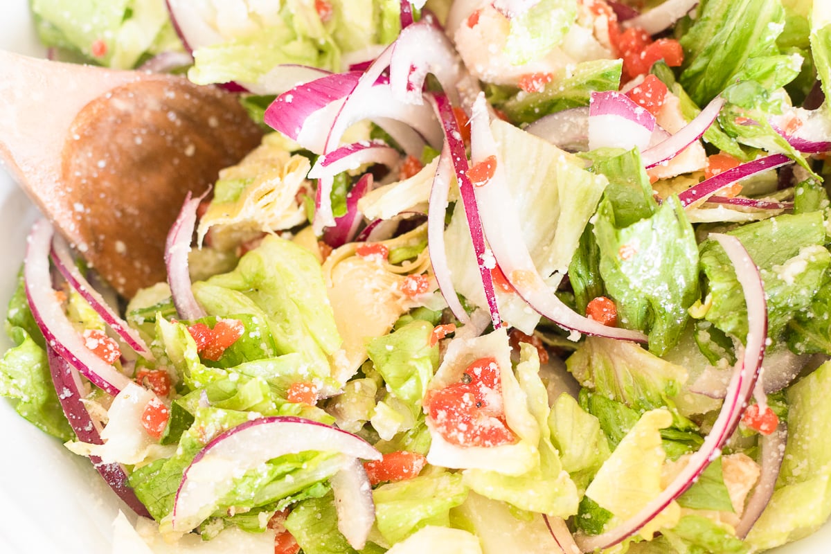 A close-up of a fresh Italian garden salad with red onions, tomatoes, and a bread roll.