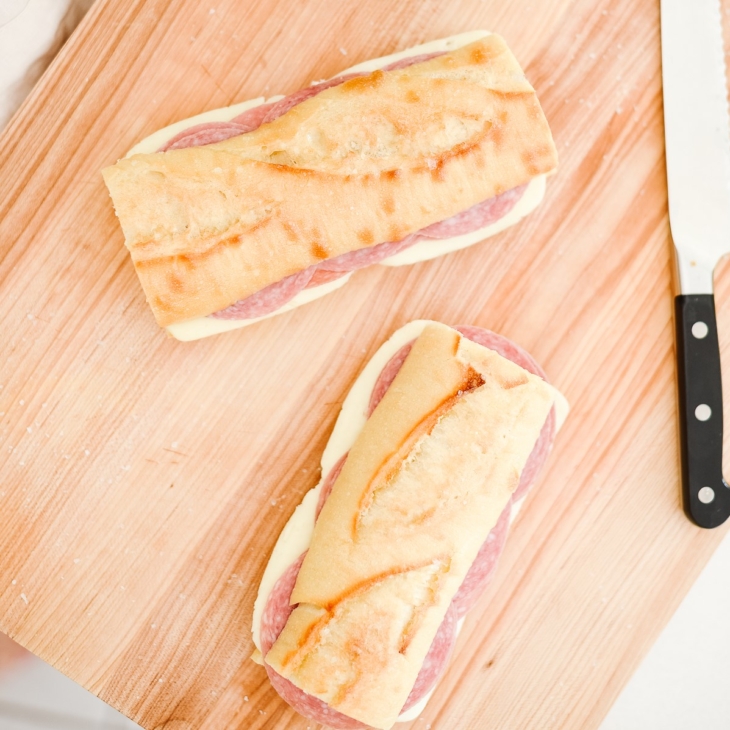 Picnic sandwiches on crusty bread, on a wooden cutting board with a knife to the side.