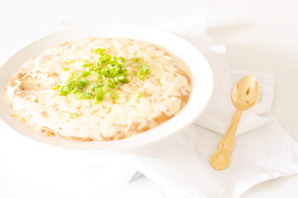 A white bowl full of cream cheese bean dip, topped with diced chives and gold spoon to the side