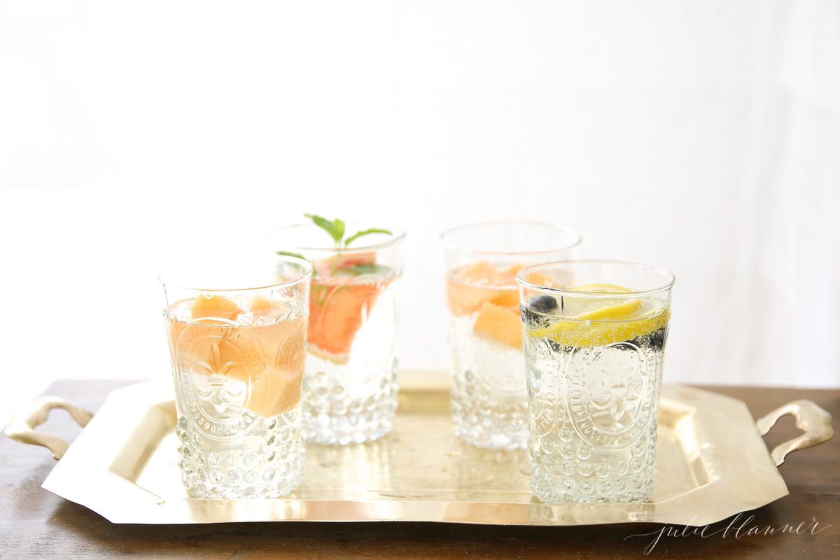 Glasses full of fruit infused water recipes on a gold tray.