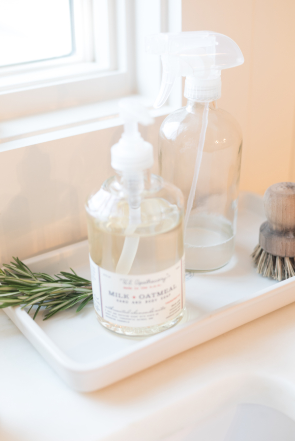 A kitchen sink with a bottle of marble cleaner and a sprig of rosemary.