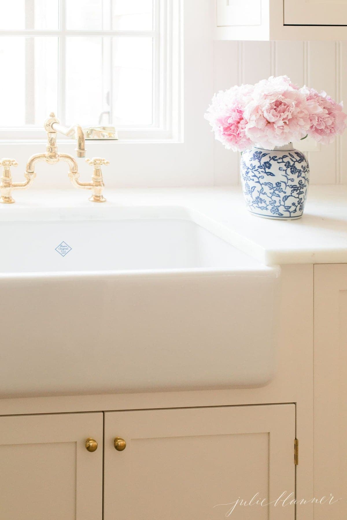 Pink peony flowers in a blue and white vase by a kitchen farm sink.