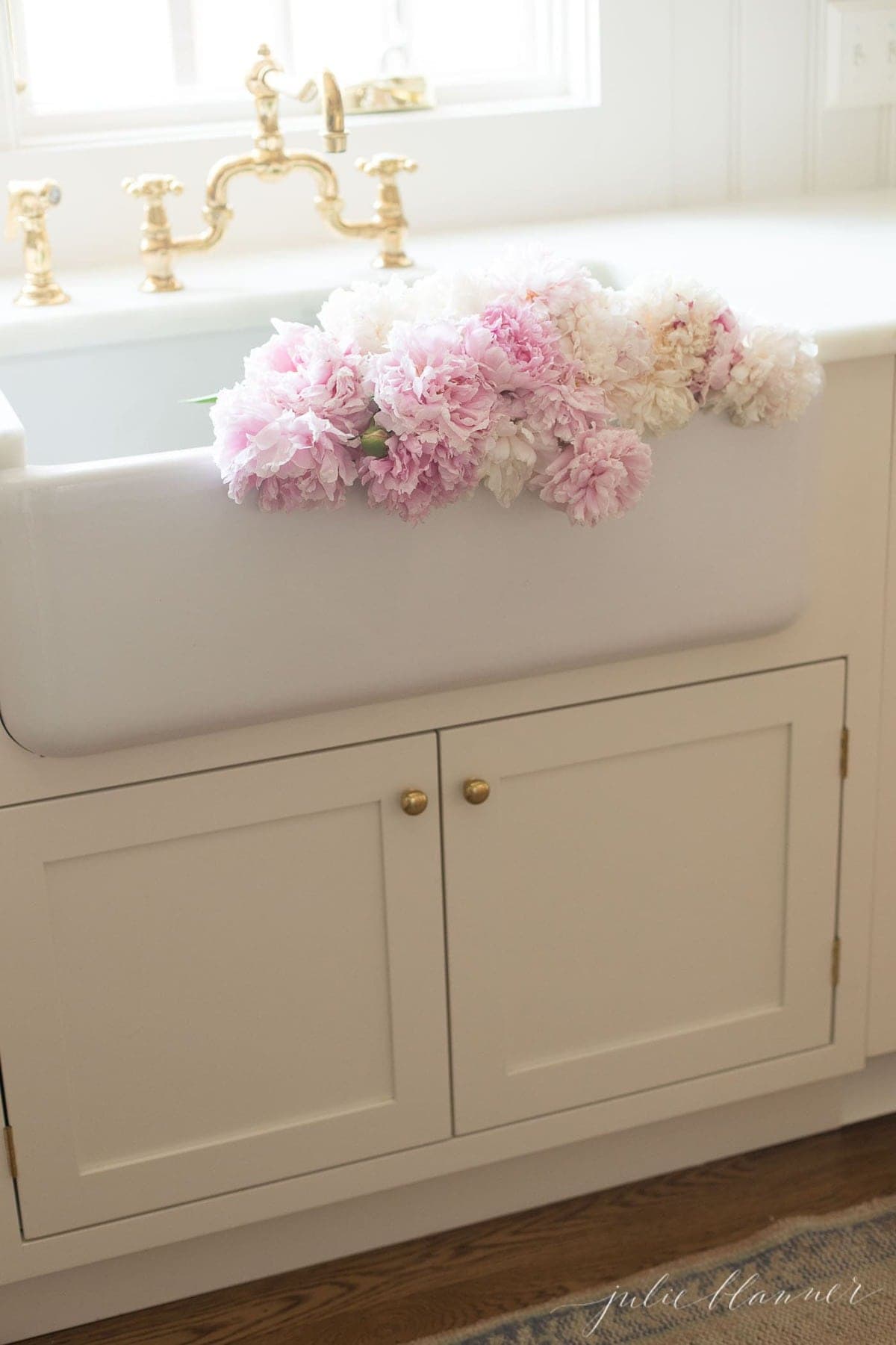 White and pink peony colors, draped over the front of a farm sink in a white kitchen.