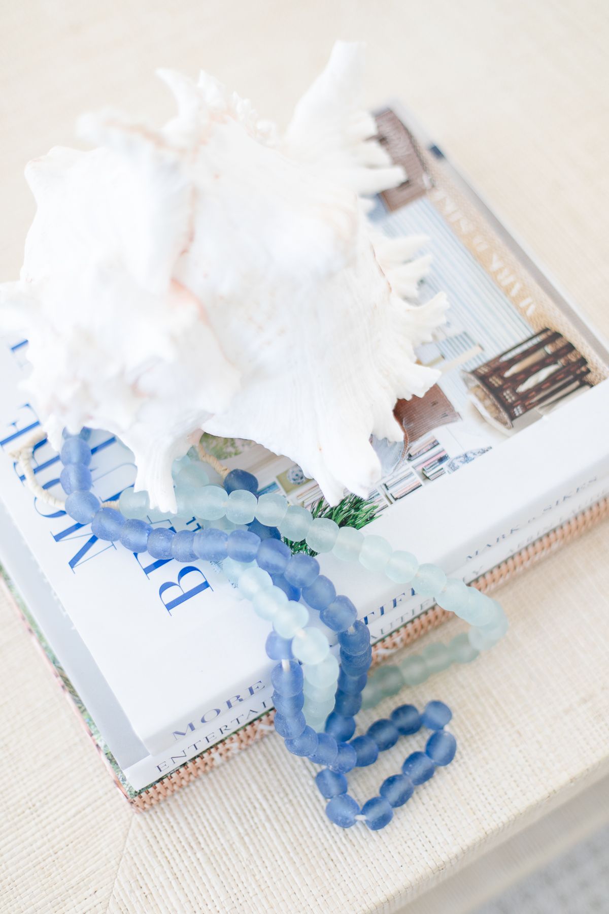 A stack of coffee table books with a sea shell and blue beads on top