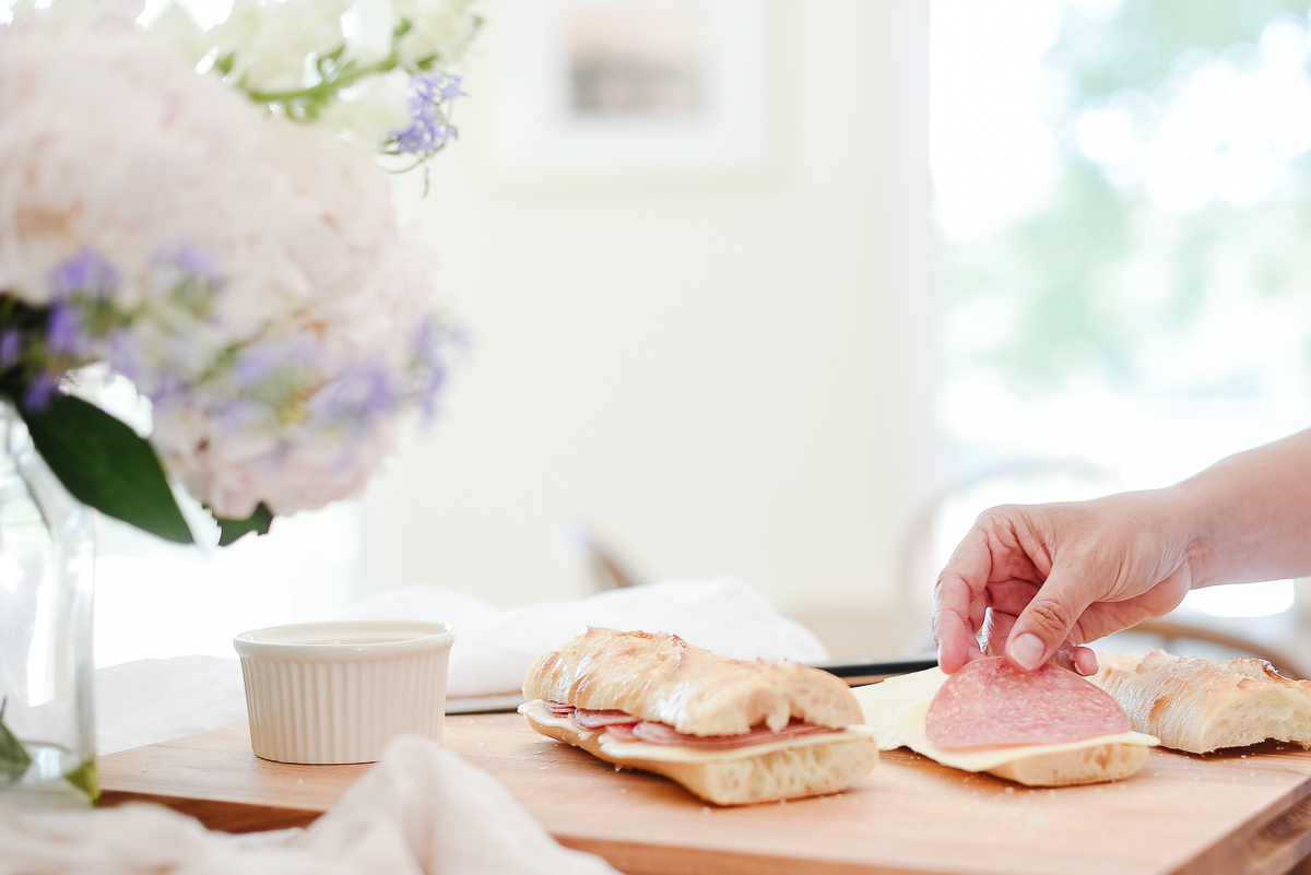Picnic sandwiches sliced on a wooden cutting board, hands creating the sandwiches.