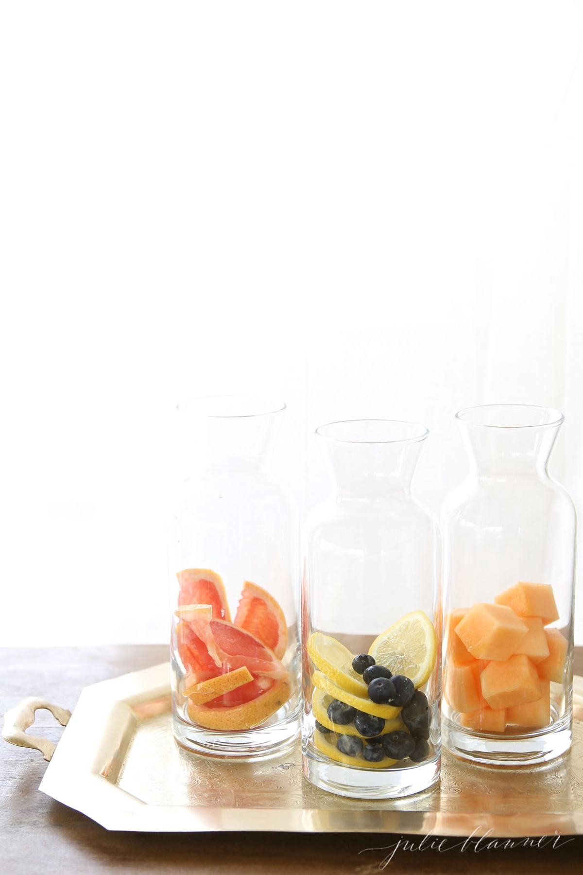 Glass containers full of fruit infused water on a gold tray.