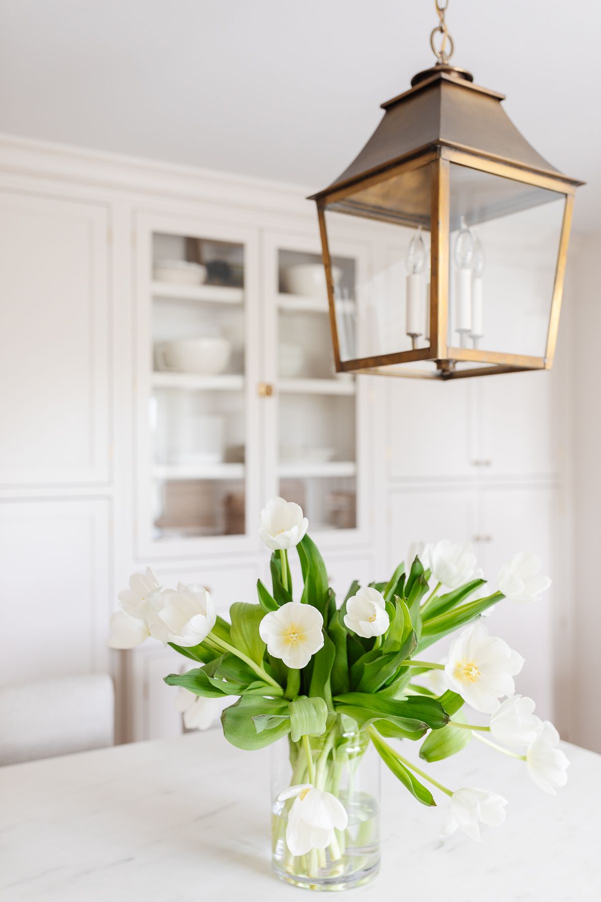 A brass pendant lantern hanging over a vase of white tulips on a kitchen island.