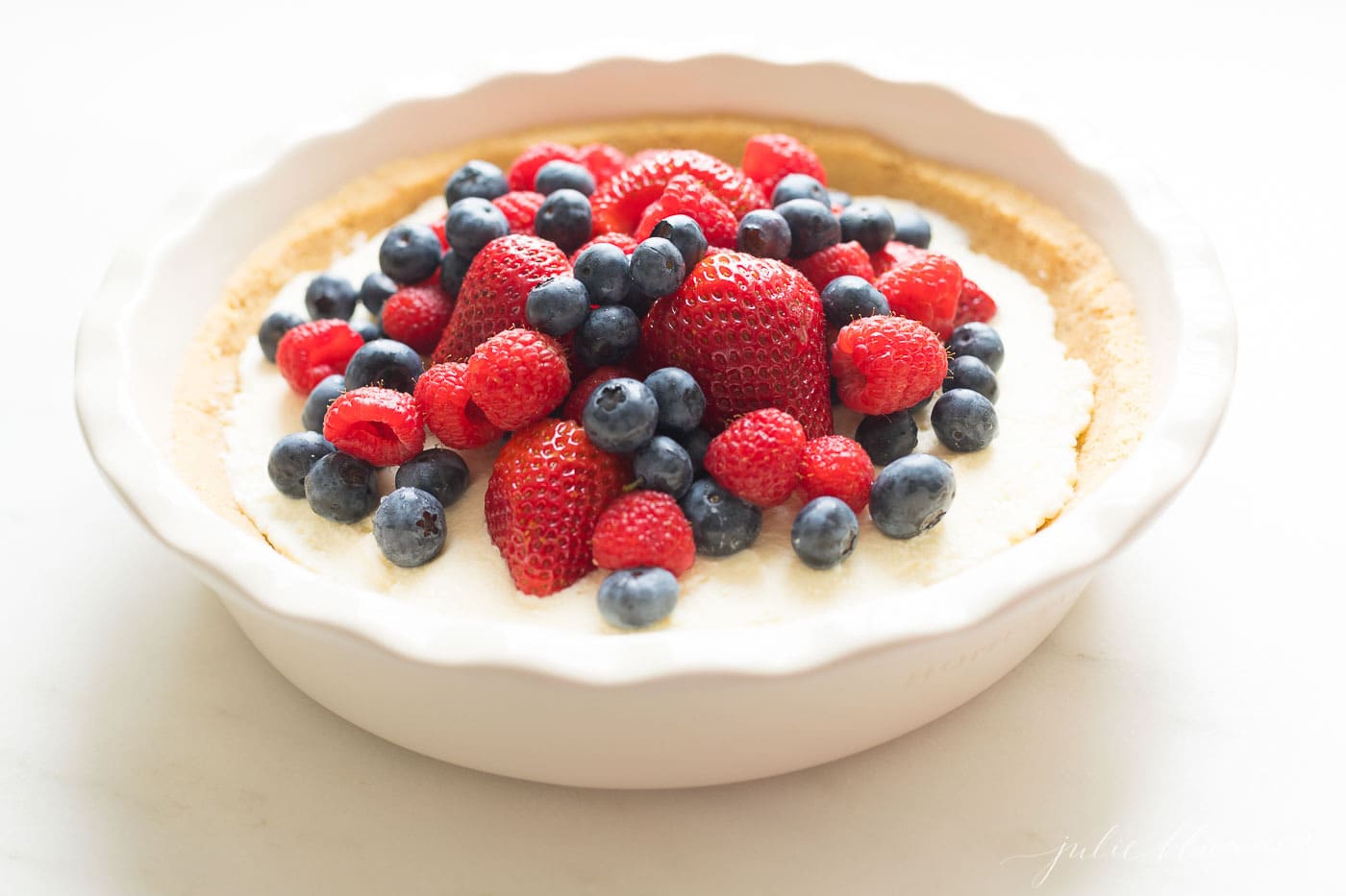 A no bake lemon pie in a white baking dish topped with fresh berries