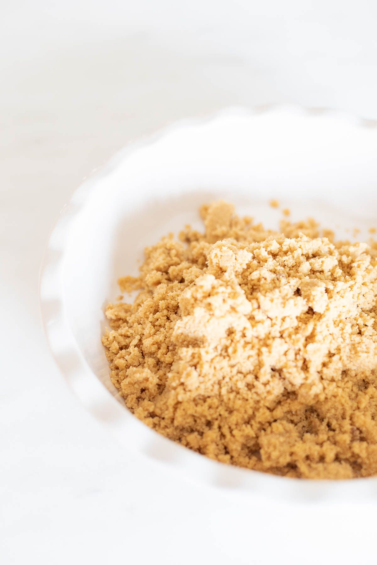 Ingredients for a no bake shortbread crust in a white ruffled ceramic pie dish