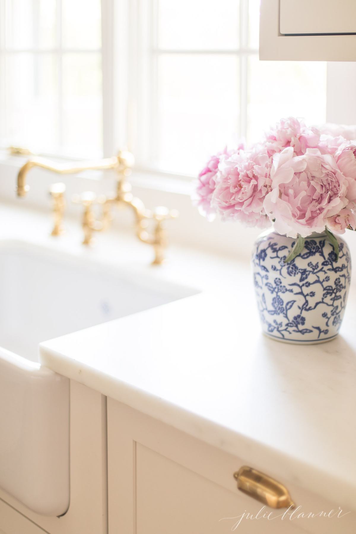 A blue and white porcelain vase of pink peonies by the kitchen sink.