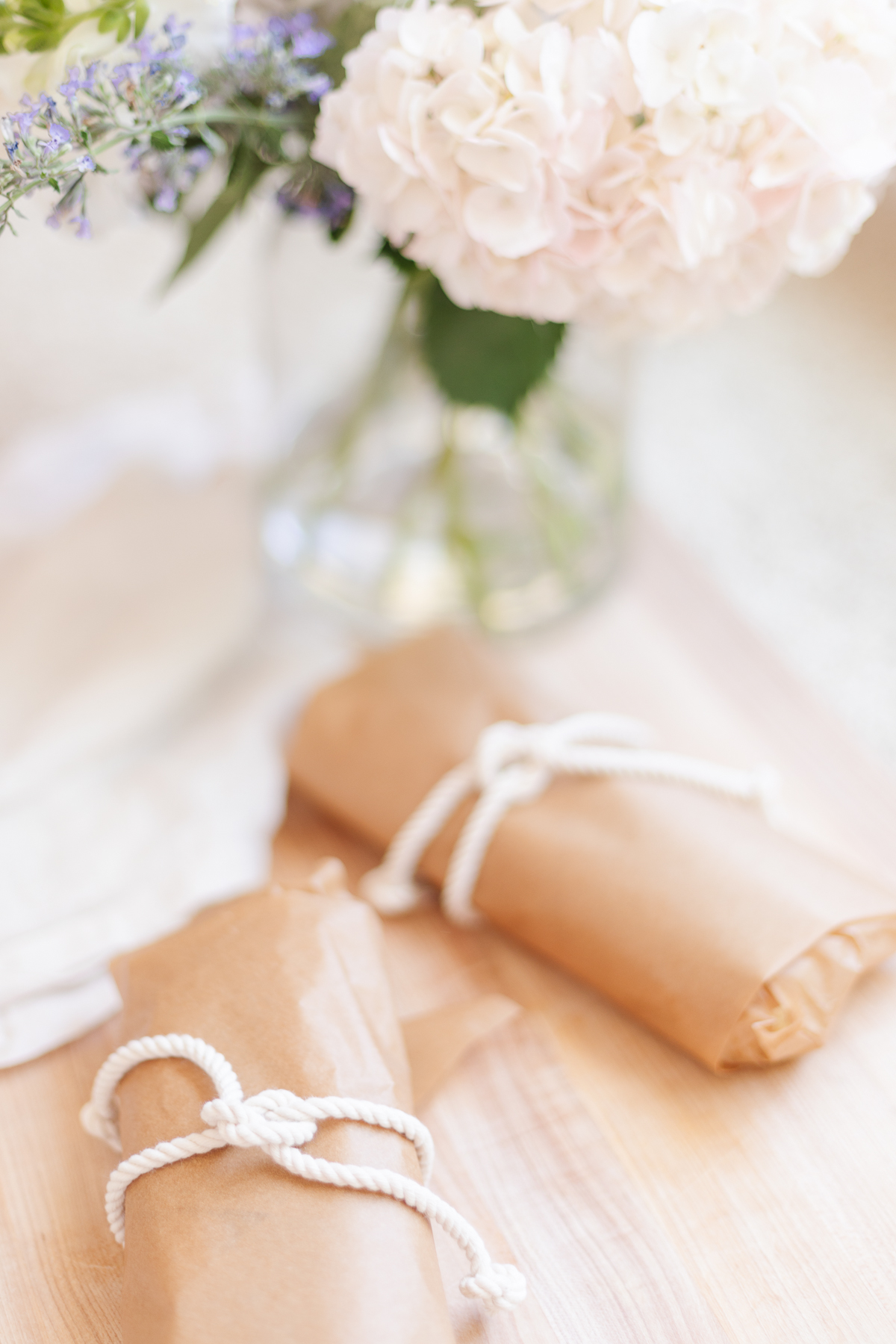 Picnic sandwiches on a wooden cutting board, wrapped in brown paper with a white string.