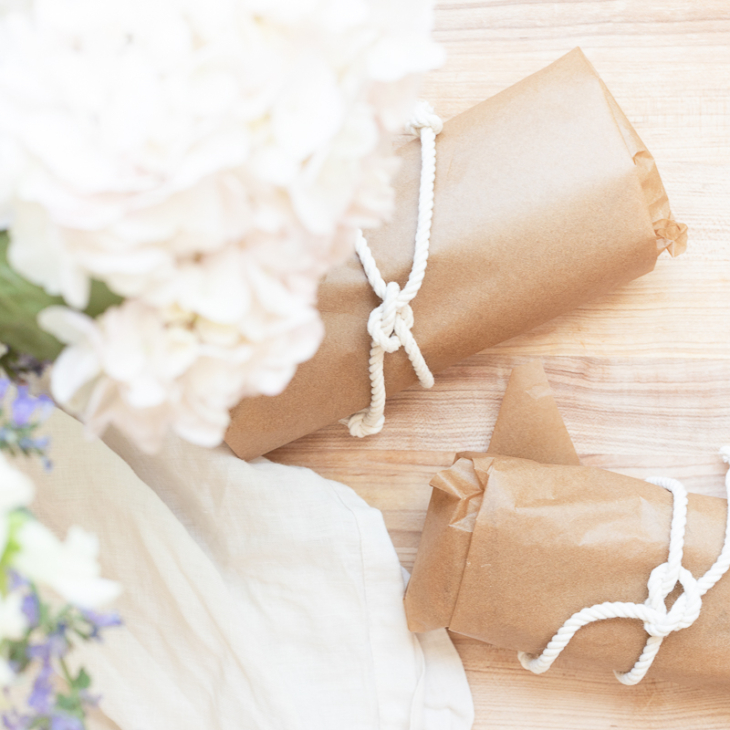 Picnic sandwiches on a wooden cutting board, wrapped in brown paper with a white string.