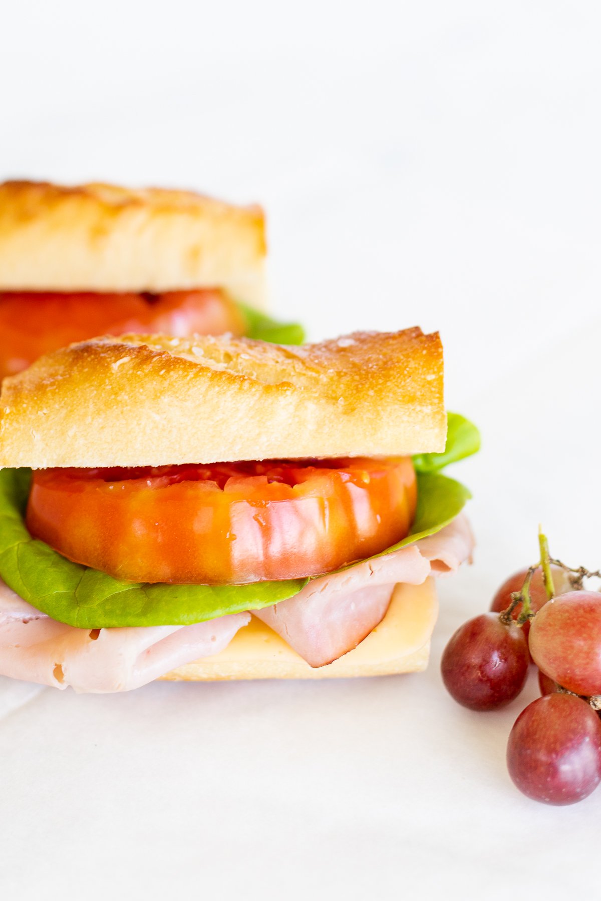 A picnic sandwich with ham, tomatoes, lettuce and grapes.