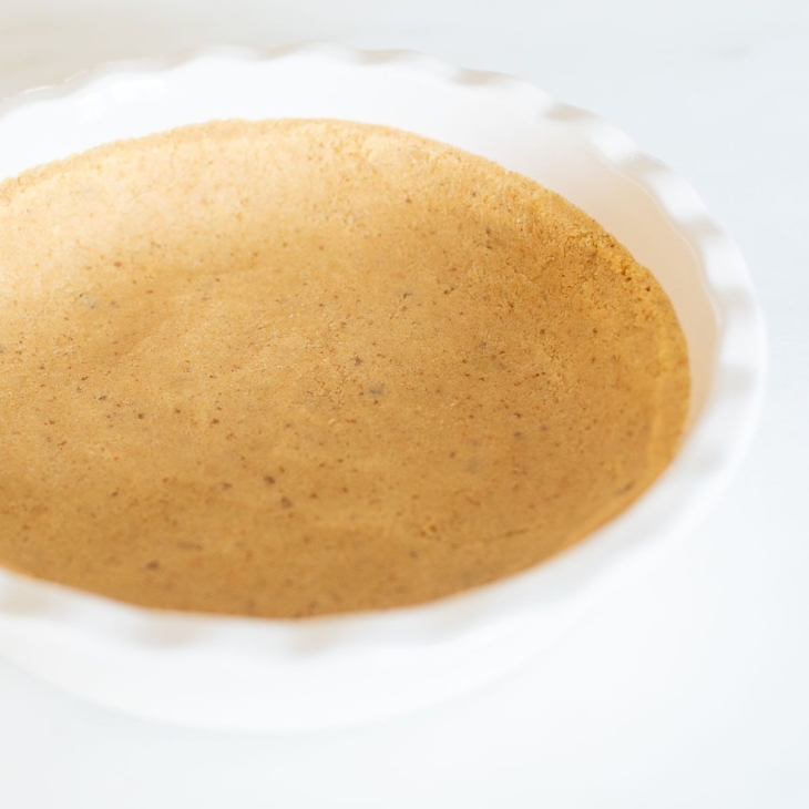 A shortbread crust pressed into a white ruffled ceramic pie dish on a marble surface