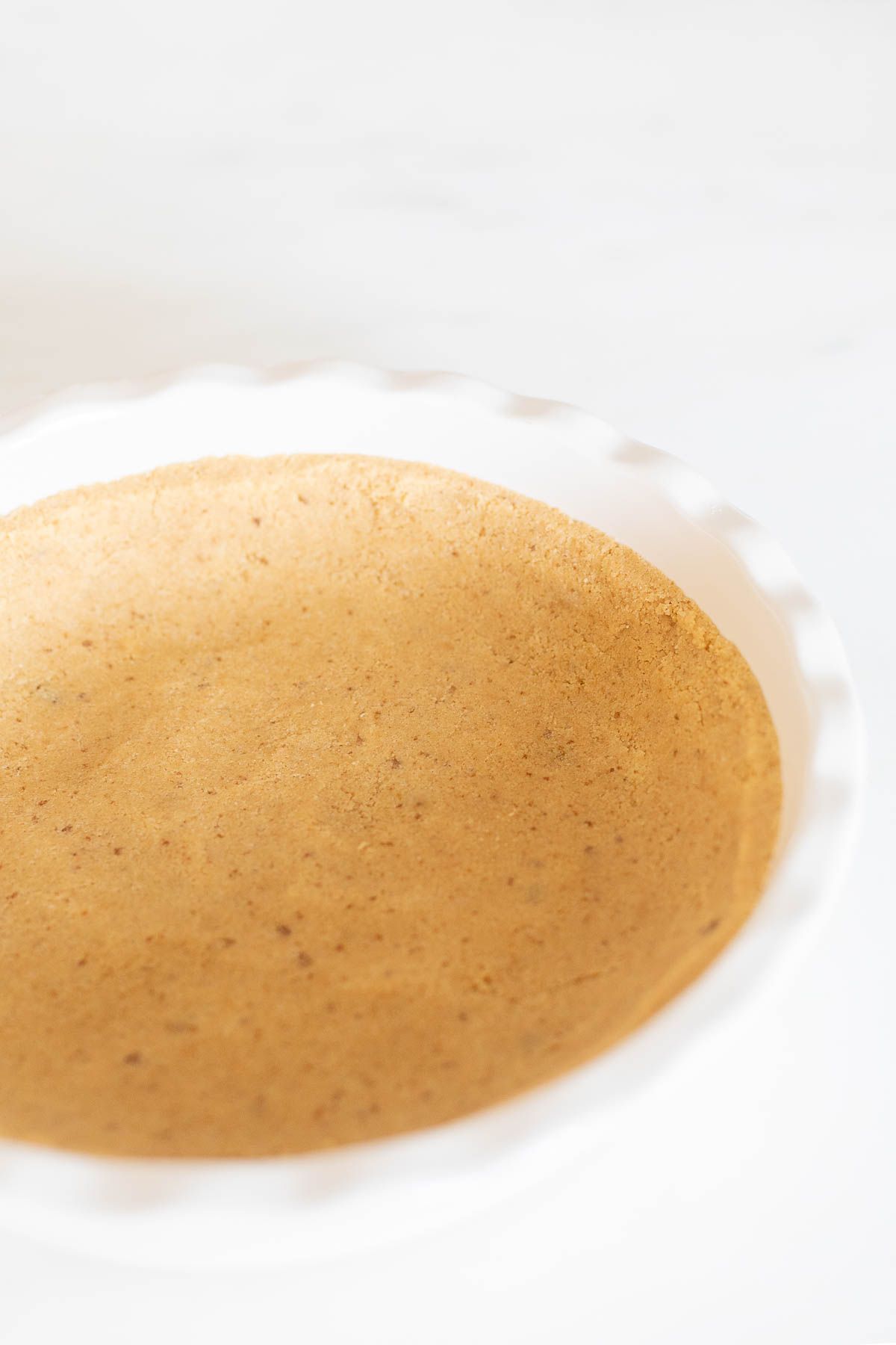 A shortbread crust pressed into a white ruffled ceramic pie dish on a marble surface