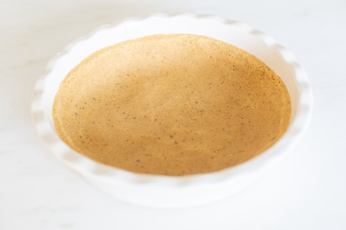 A shortbread crust pressed into a white ruffled ceramic pie dish on a marble surface